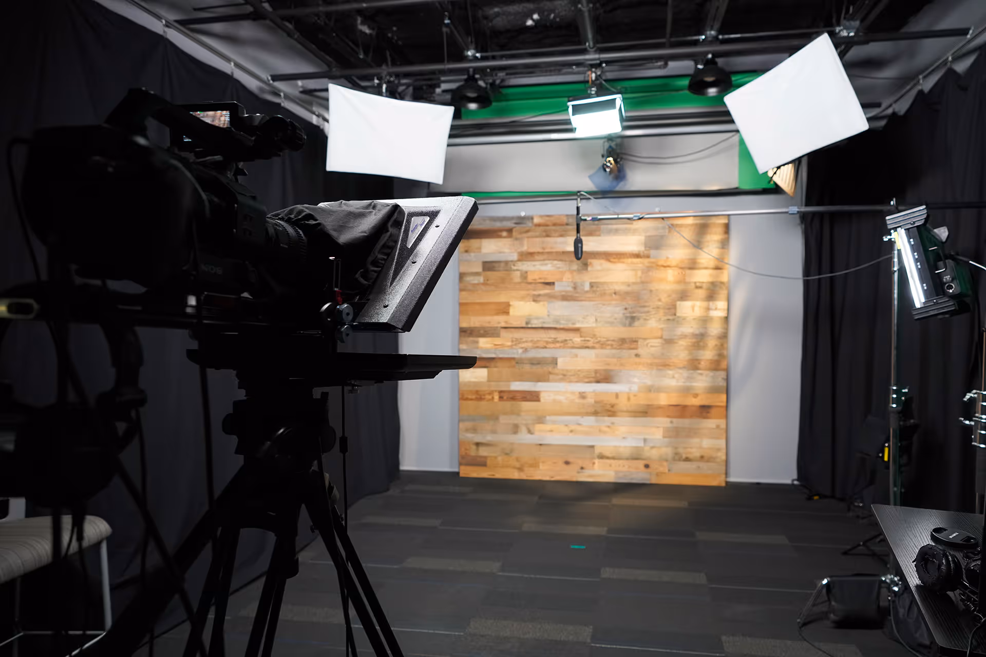 Professional video studio with camera, teleprompter, lighting equipment, and wooden panel backdrop.